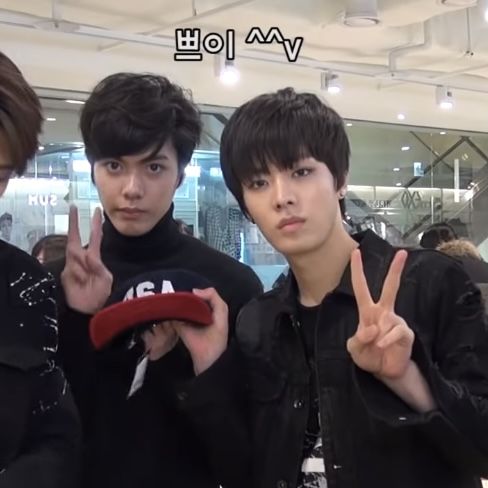 three young men standing next to each other in front of a store window holding up peace signs