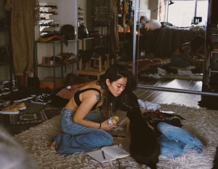 a woman is sitting on the floor with her cat and looking at something in front of her