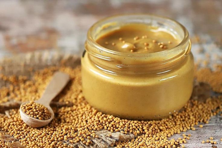 a jar of mustard sitting on top of a table next to a spoon and some seeds