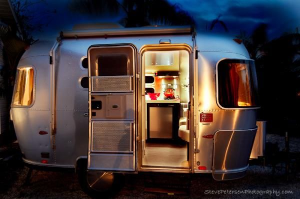 an airstream is lit up at night with its door open and the interior lights on