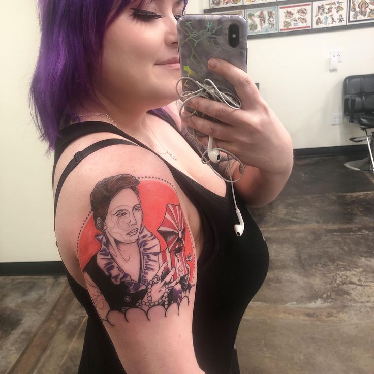 a woman with purple hair and tattoos on her arm taking a selfie in the mirror