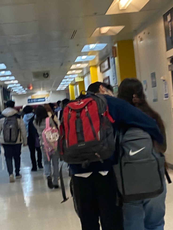 many people are walking down the hallway with backpacks on their backs and one is carrying a book bag