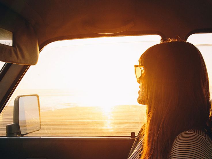 a woman sitting in the back seat of a car looking out at the ocean and sunset