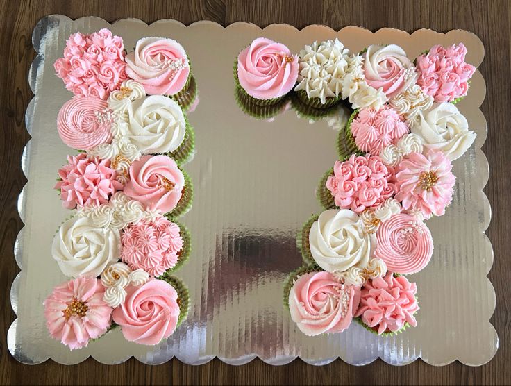 a cake decorated with pink and white flowers on top of a silver plate, sitting on a wooden table