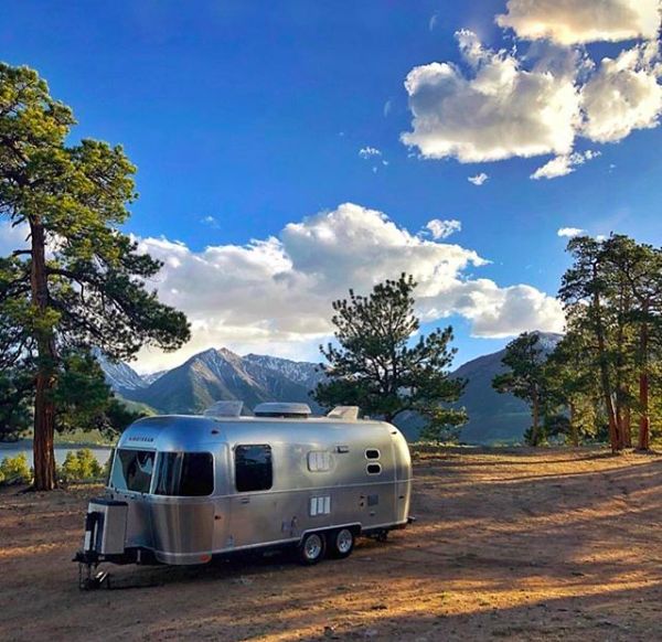 an airstream parked on the side of a dirt road in front of trees and mountains