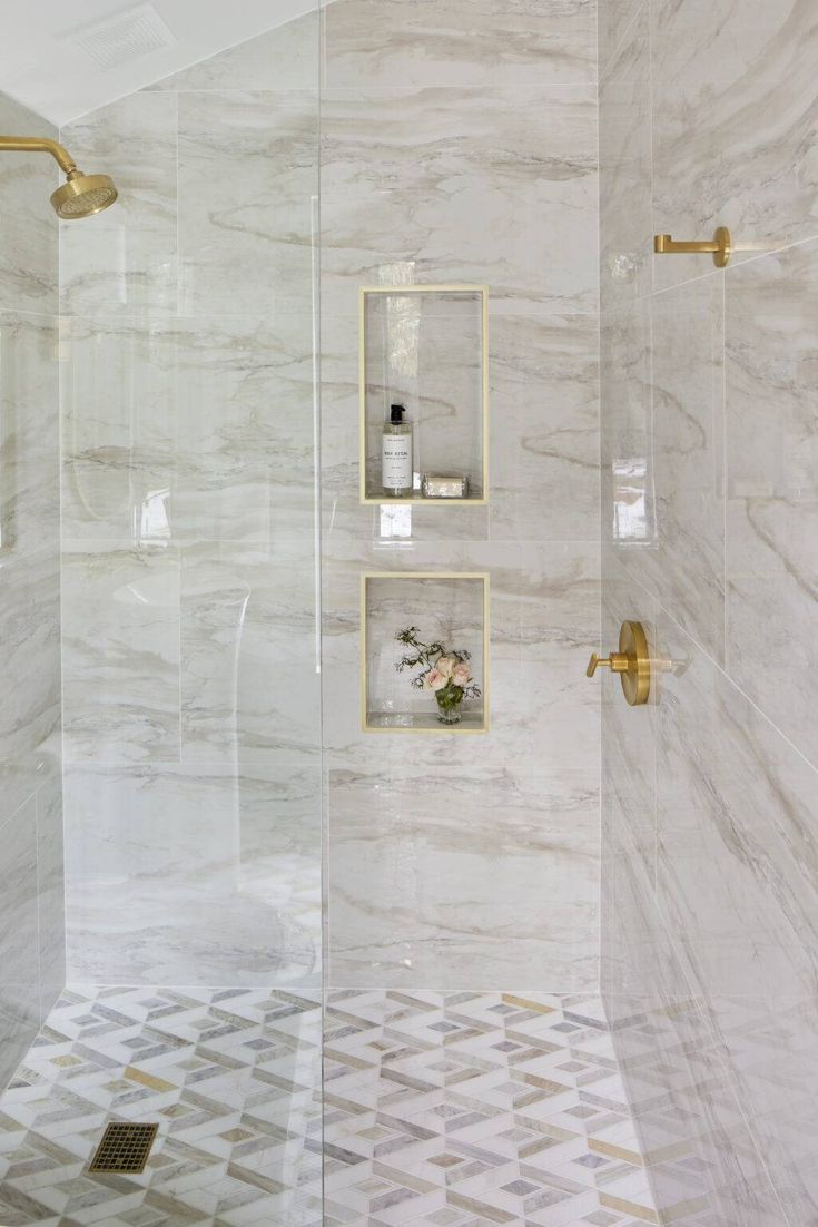 a bathroom with white marble walls and gold fixtures on the shower head, glass door, and tiled floor