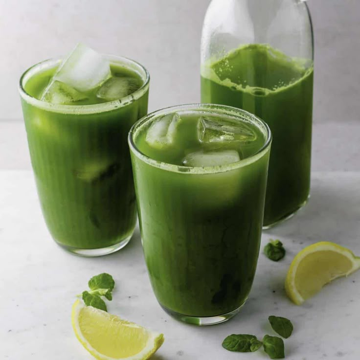 two glasses filled with green smoothie next to sliced lemons