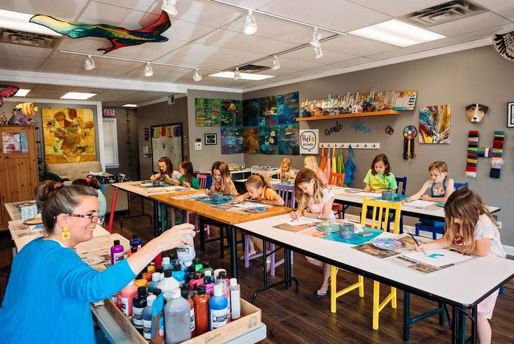 a group of children sitting at desks in a room with art supplies on the tables