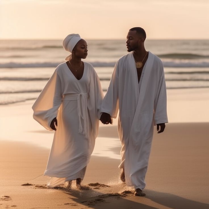 two people dressed in white walking on the beach