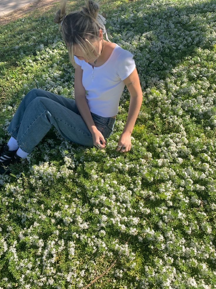 a woman sitting in the middle of a field with white flowers on her head and legs