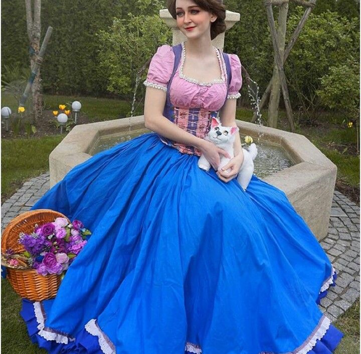 a woman in a blue dress is sitting on a bench with a cat and flowers