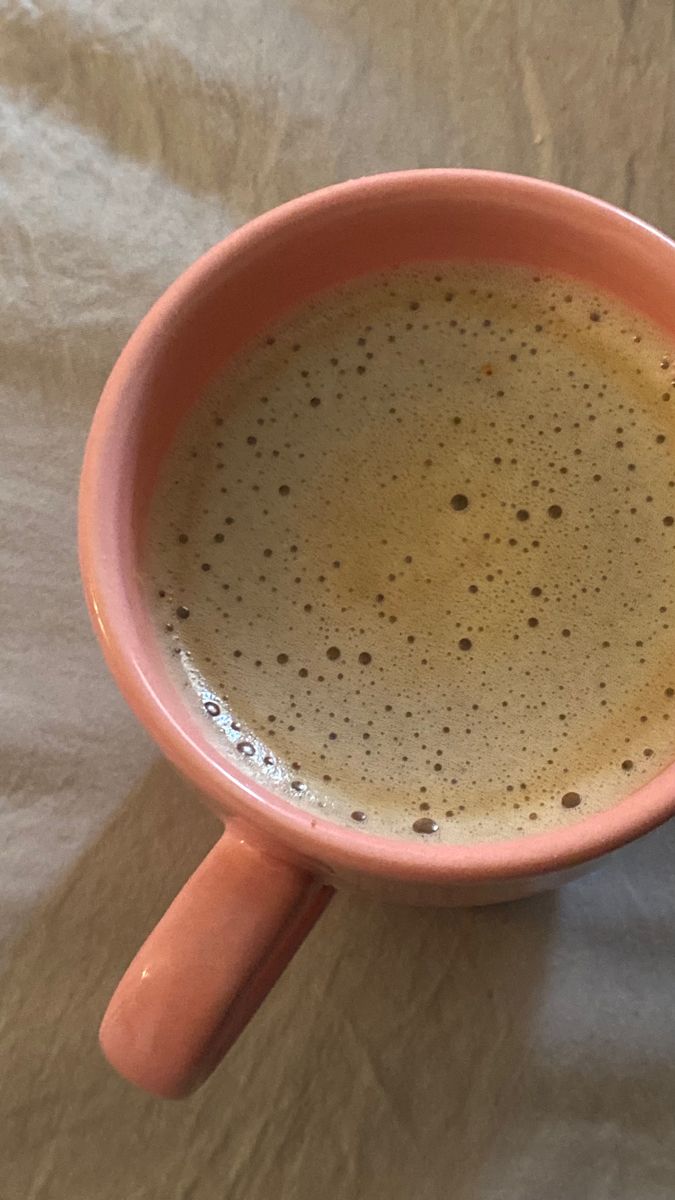 a cup of coffee sitting on top of a white tablecloth covered table with brown spots