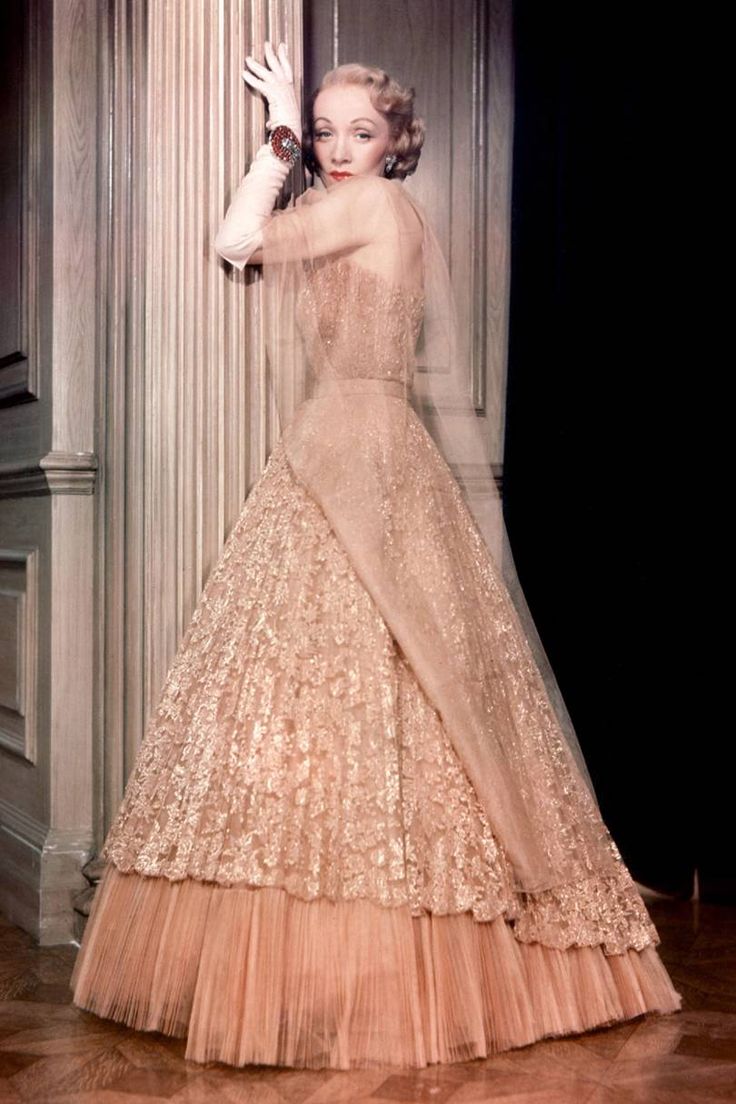 an old fashion photo of a woman in a gown and hat with her hand up to the side