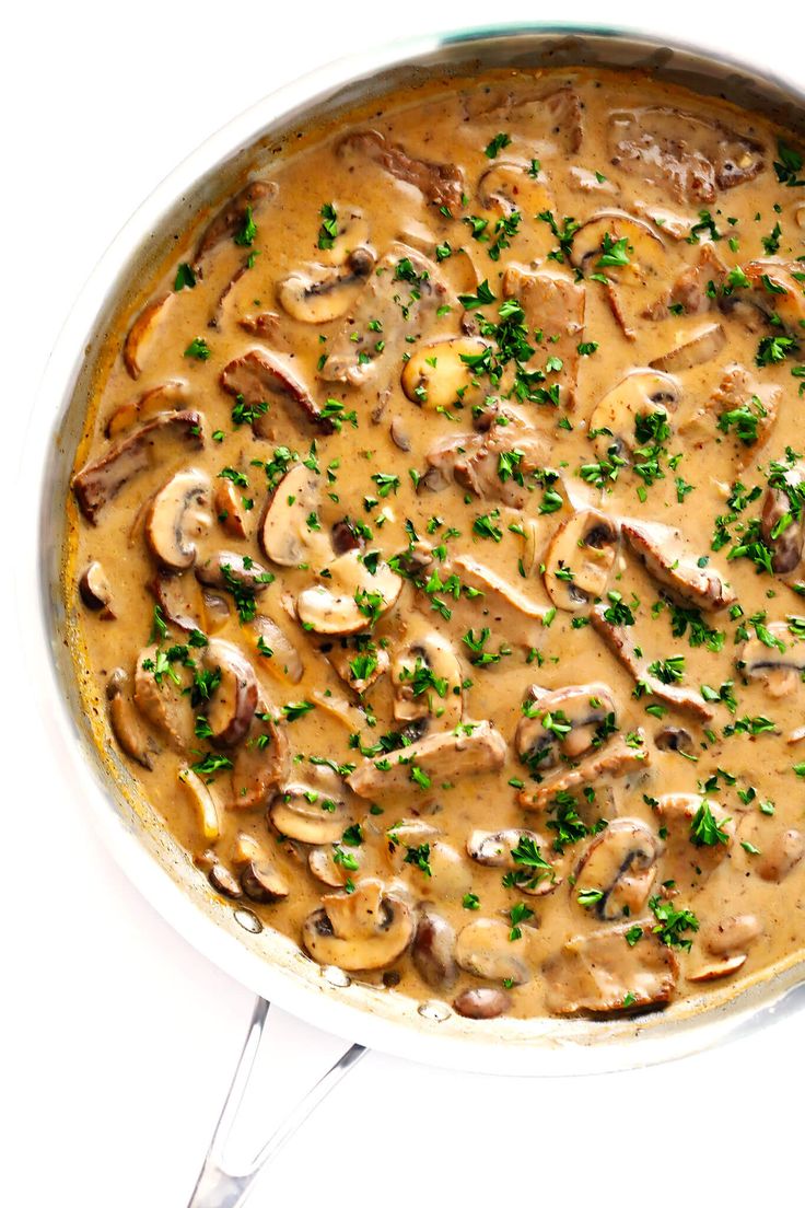 a skillet filled with mushrooms and gravy on top of a white table