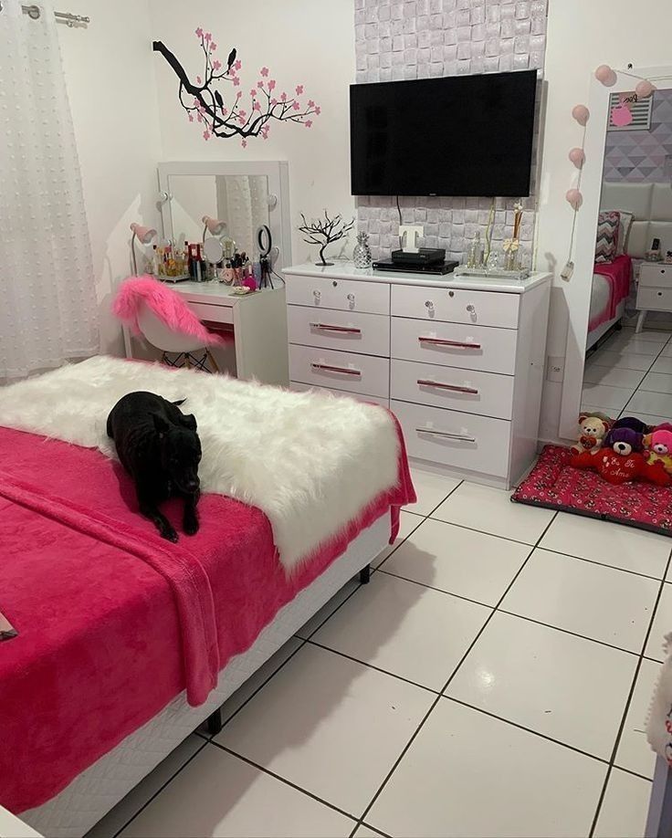 a black cat laying on top of a pink bed in a room with white furniture