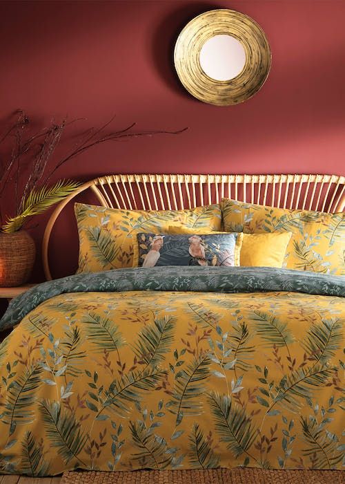 a bed with yellow comforter and pillows in a room that has red walls, wooden headboard, and round mirror on the wall