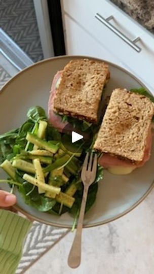 a person holding a plate with two sandwiches on it and a salad in front of them