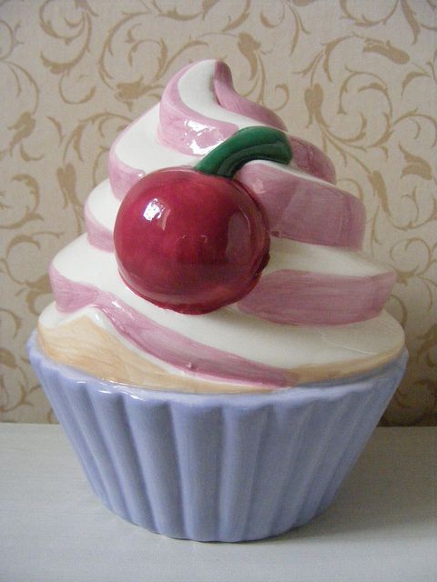 a cupcake with a cherry on top is sitting in front of a wallpapered background