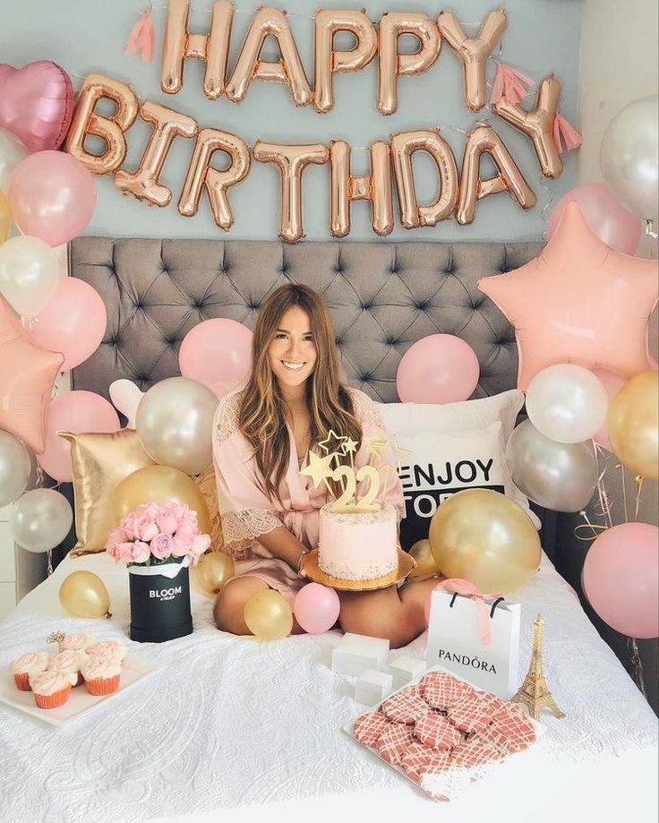 a woman sitting on top of a bed with a cake in front of her and balloons around her