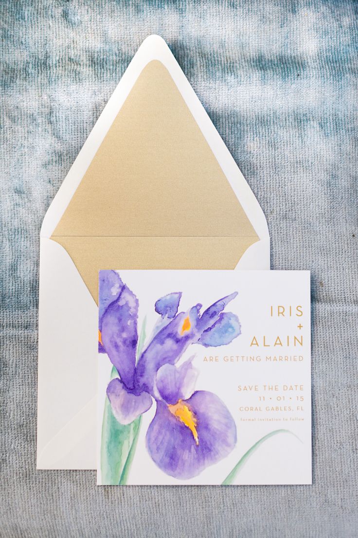 an open envelope with purple irises and gold foil on the inside, sitting on a blue background