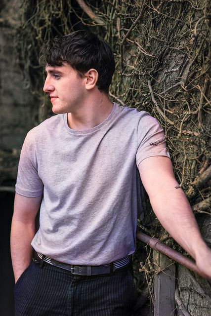 a young man leaning against a wall with vines on it