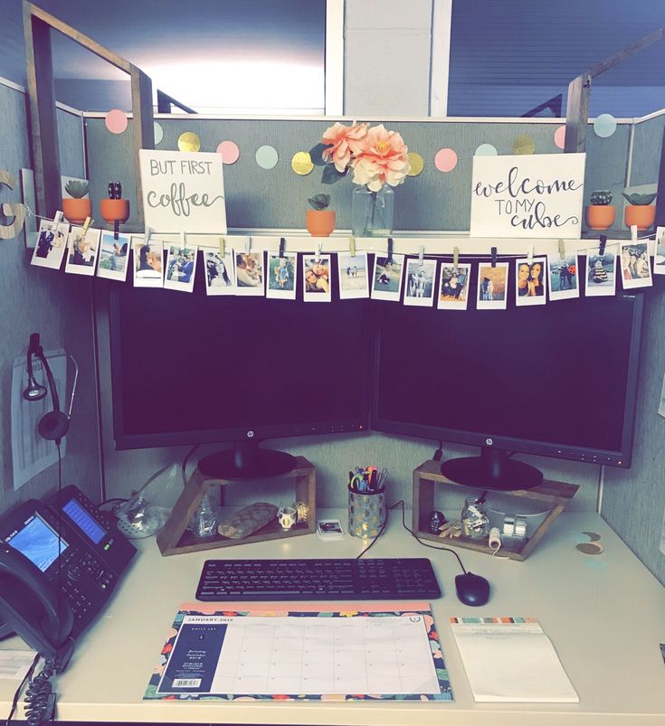 an office cubicle with two computer monitors and pictures on the wall