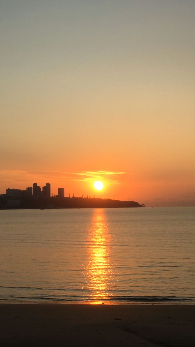 the sun is setting over the ocean with buildings in the background