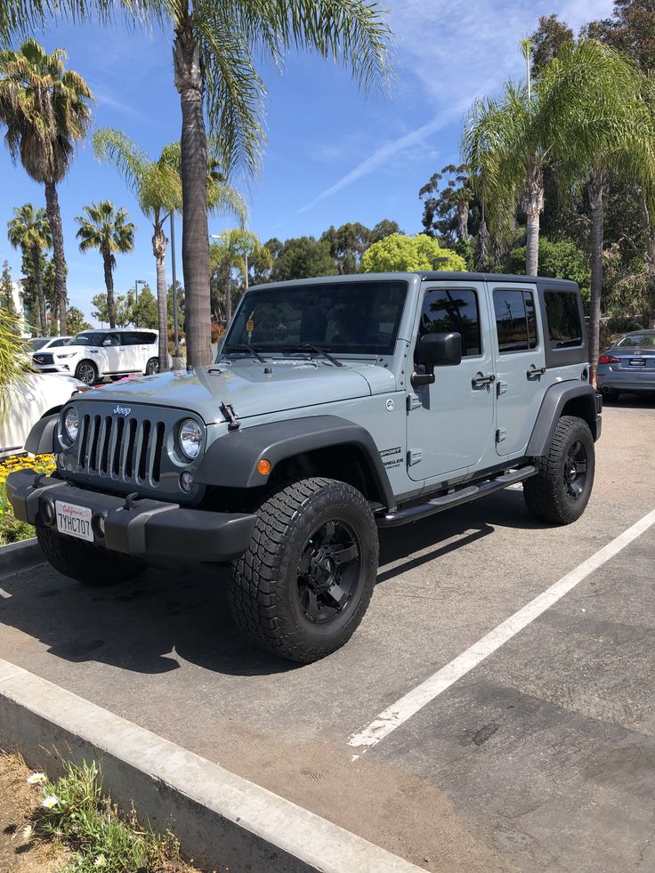 a gray jeep parked in a parking lot next to palm trees and other cars on the street