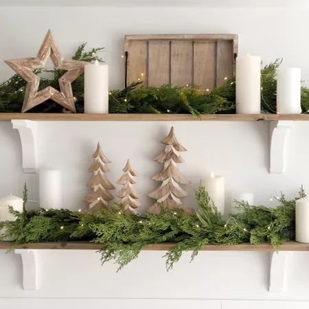 two wooden christmas trees on shelves with candles and greenery