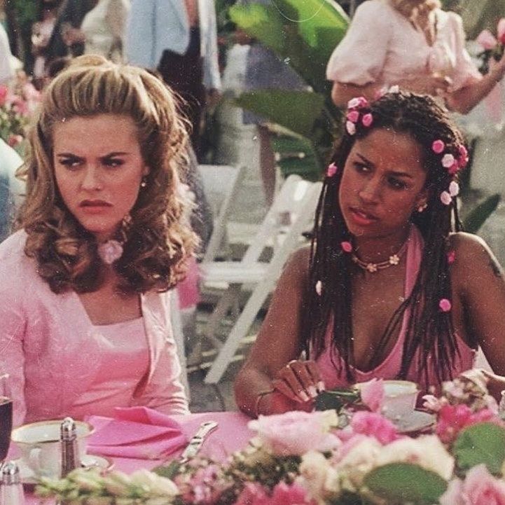 two women sitting at a table with pink flowers in their hair and one woman wearing a pink dress