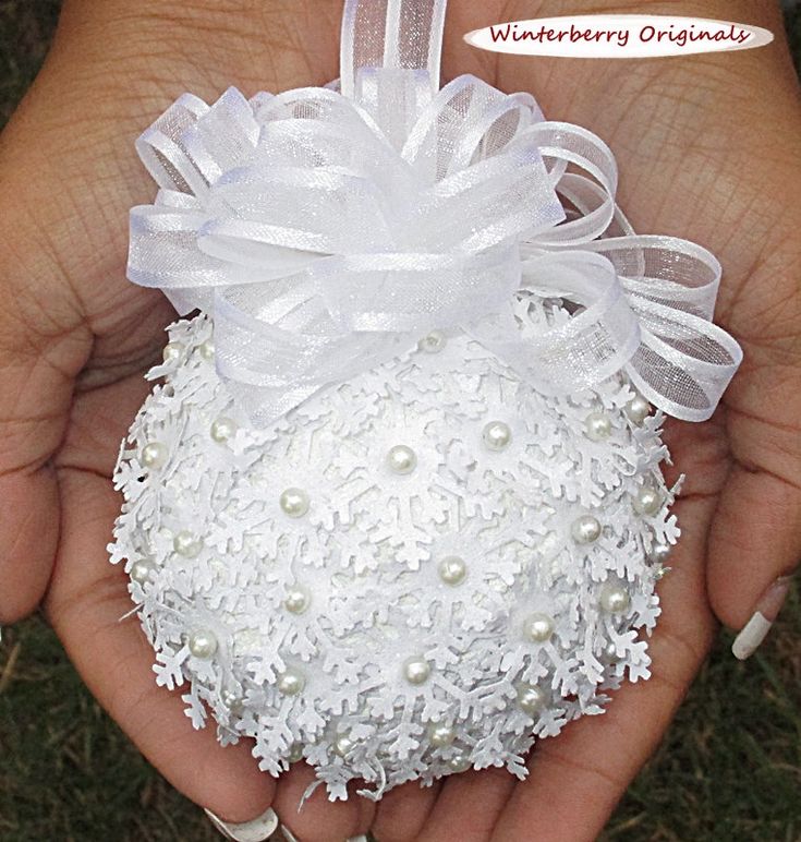 a hand holding a white ornament with pearls and ribbon on it's side