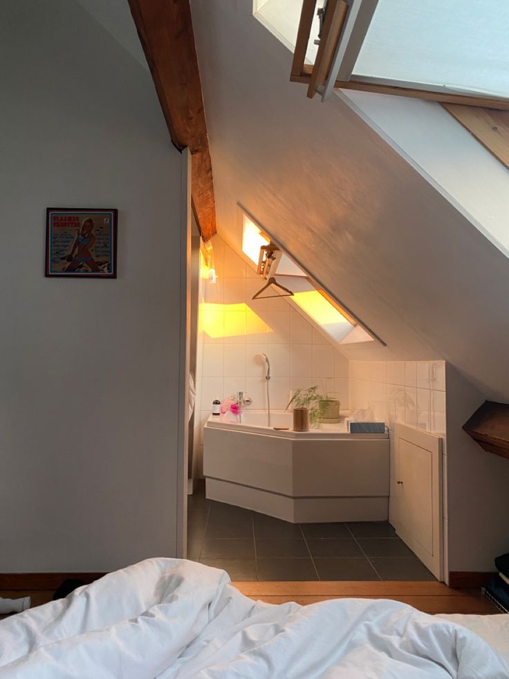 an attic bedroom with white bedding and exposed wood beams, is shown from the doorway