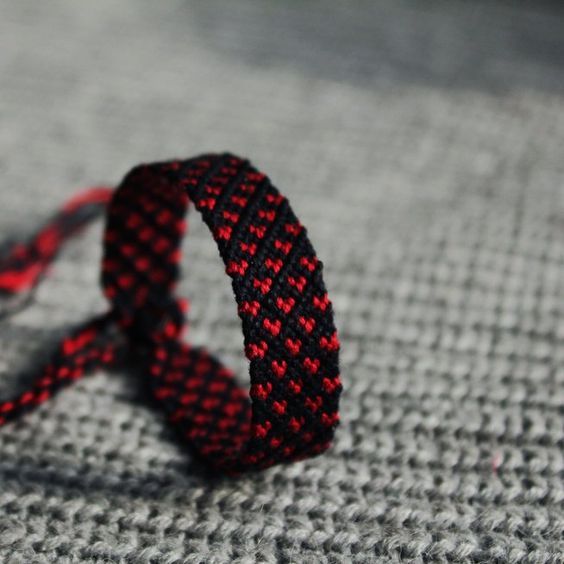 a red and black bracelet sitting on top of a gray blanket