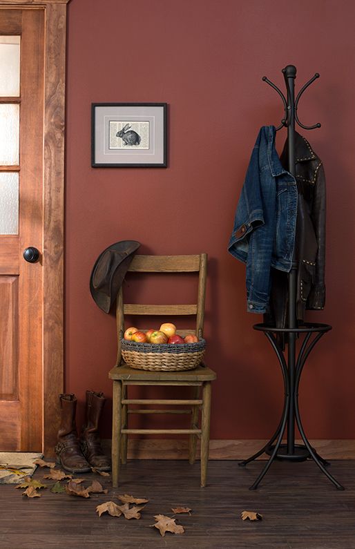 a wooden chair next to a coat rack with apples on it and an apple basket