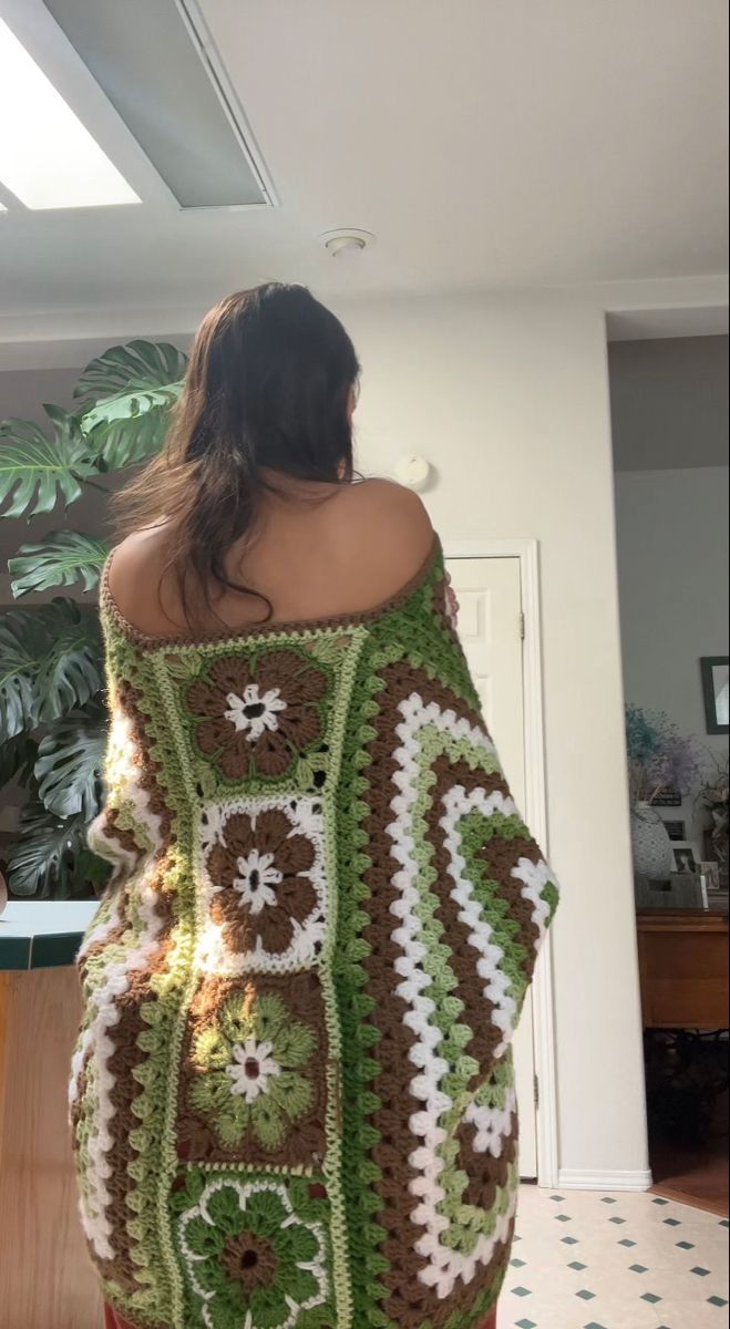 a woman is wearing a crocheted green and white sweater with flowers on it