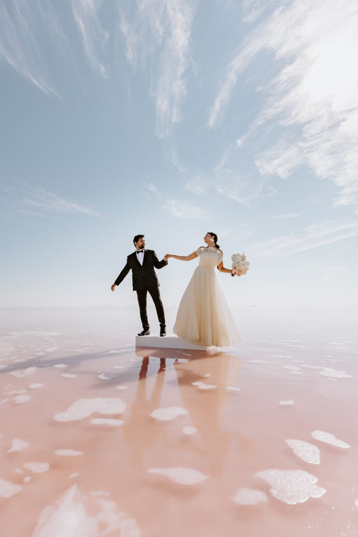 a bride and groom are holding hands in the middle of a salt flat with footprints on the ground