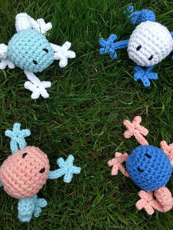 four crocheted toys are laying on the grass together, one is blue and one is pink