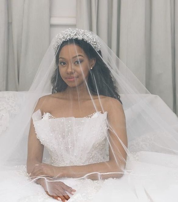 a woman in a wedding dress sitting on a bed with her veil over her head