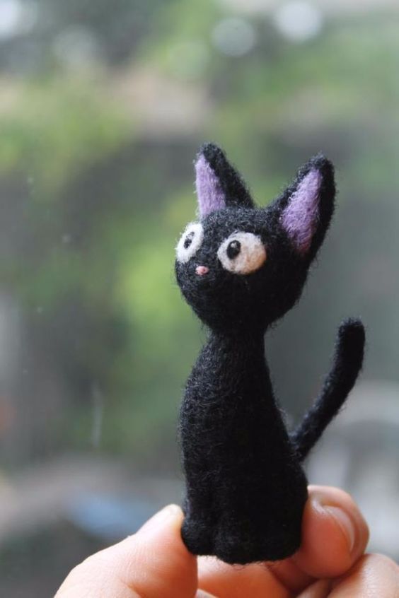 a hand holding a tiny black cat with eyes on it's face and tail