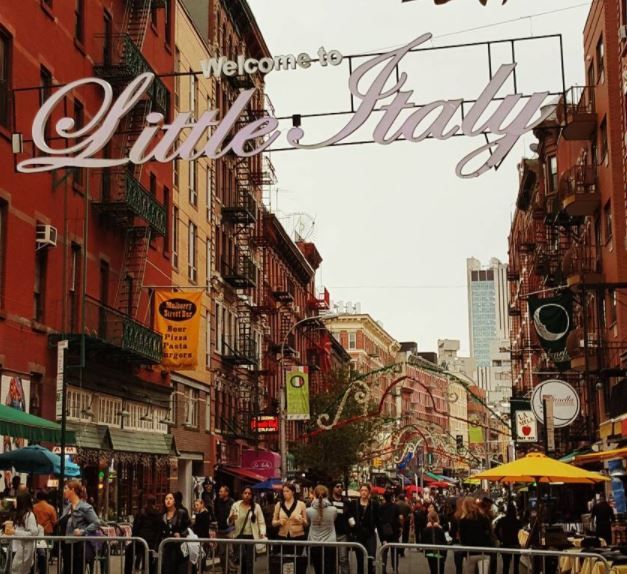 people are walking down the street in front of some buildings and signs that say little italy