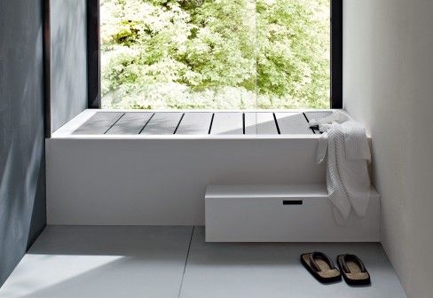 there is a bathroom with a large window above the bathtub and slippers on the floor