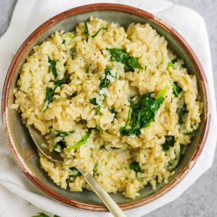 a bowl filled with rice and spinach on top of a white cloth next to a spoon