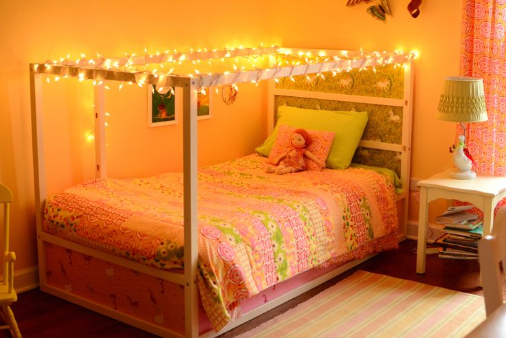 a bedroom decorated in pink and green with lights on the bed, rugs and table