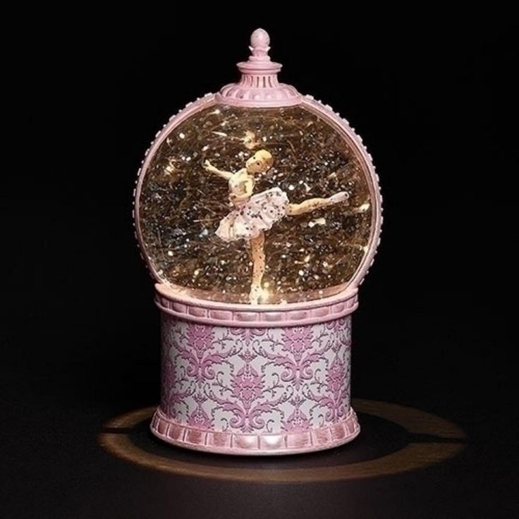 a snow globe with a ballerina figure in it on a black background, surrounded by lights