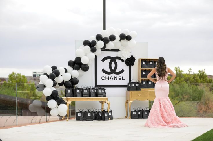 a woman standing in front of a chanel sign with black and white balloons on it