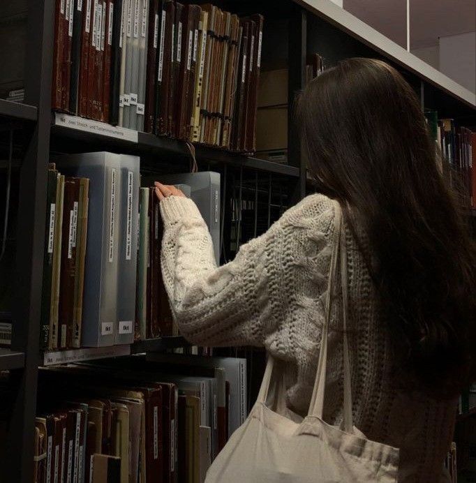 a woman is picking up books from a book shelf in a library with several shelves full of books