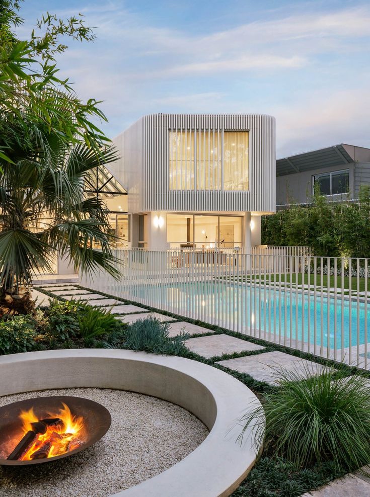 an outdoor fire pit in front of a house with a swimming pool and palm trees