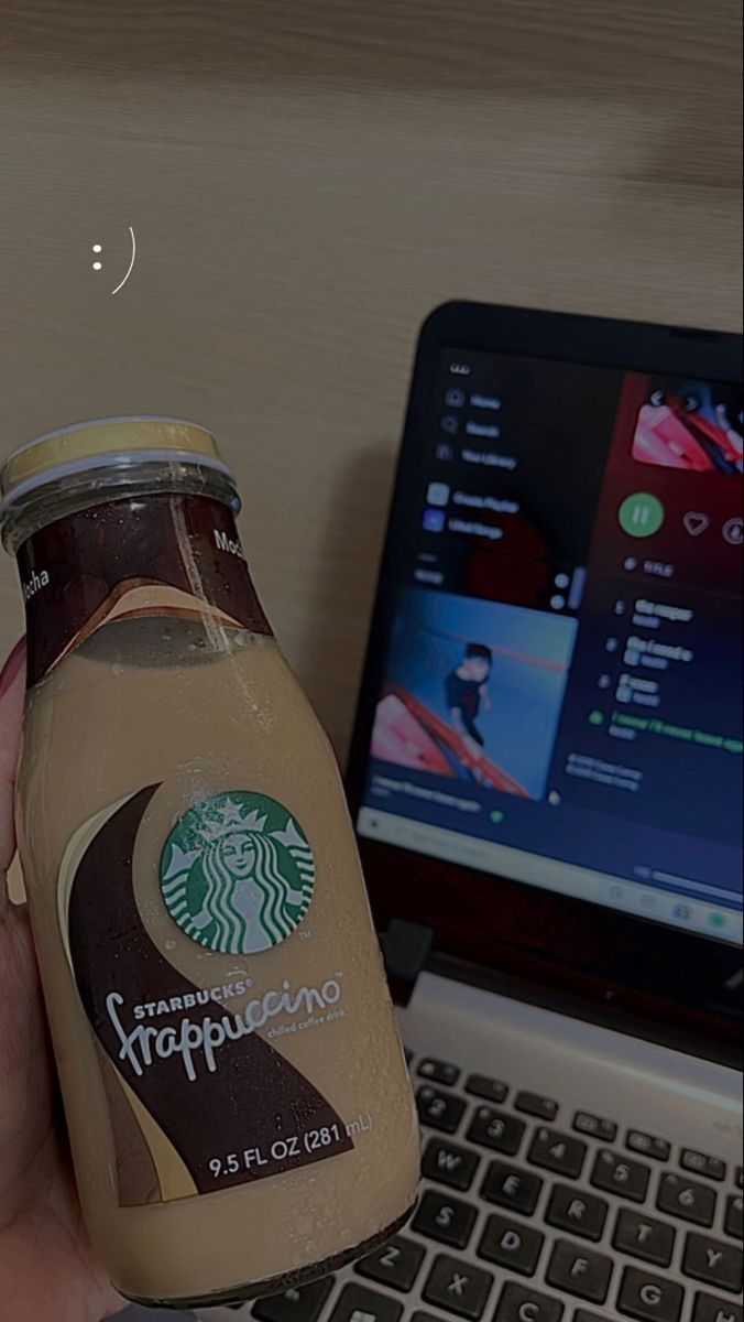 a person is holding a bottle of coffee in front of a laptop and computer keyboard