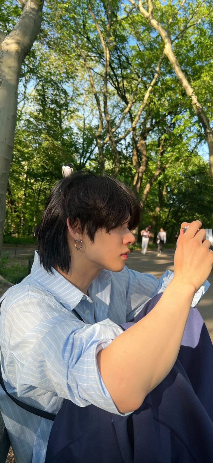 a woman sitting on a bench taking a photo with her cell phone in the park