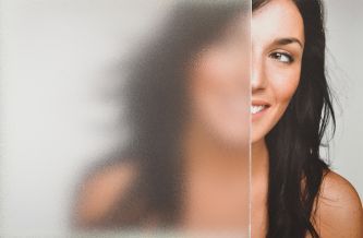 a woman with long dark hair is smiling and looking at the camera through a frosted glass door